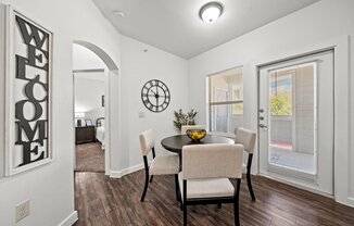A dining room with a table set for two and a welcome sign on the wall.
