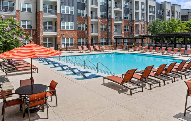 a swimming pool with chairs and an umbrella in front of an apartment building
