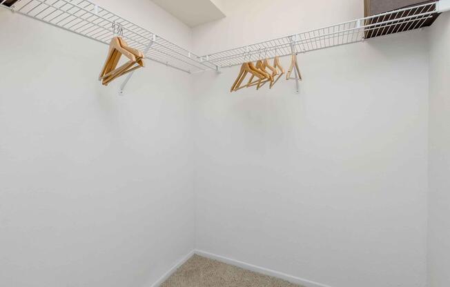 Empty closet featuring a white wire shelving unit with several wooden hangers hanging from it. The walls and floor are plain, with a soft carpet, creating a minimalistic and uncluttered space.