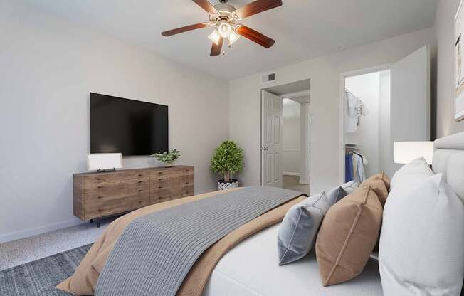 A bedroom with a bed, pillows, a ceiling fan, and a television on a wooden cabinet.