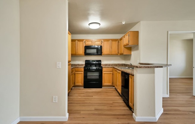 an empty kitchen with wood flooring and black appliances