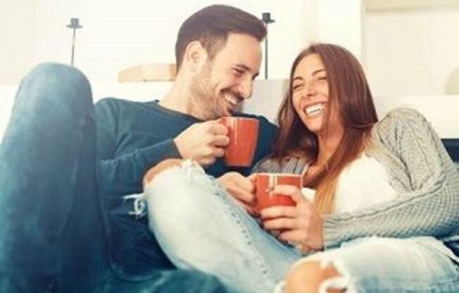 a man and woman sitting on a couch holding cups of coffee