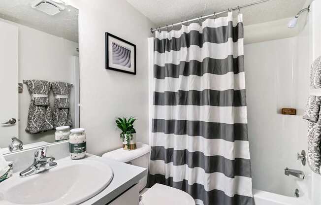 A bathroom with a striped shower curtain and a plant on the toilet.
