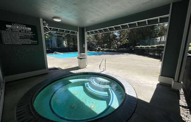A hot tub is in the middle of a patio with a pool and a sign that says pool rules.