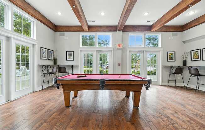 A pool table is in the middle of a room with wood floors and a high ceiling.
