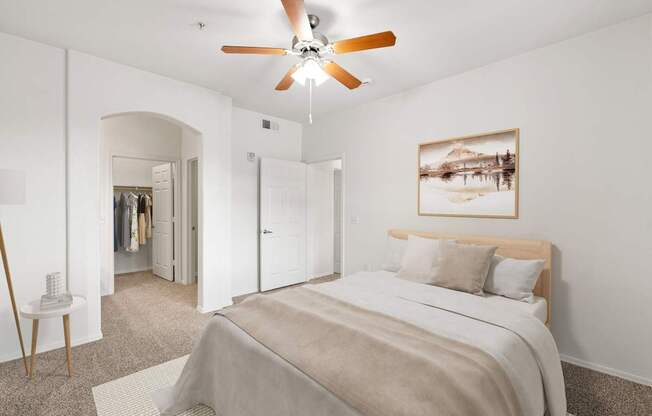 A bedroom with a bed, a ceiling fan, and a painting on the wall.
