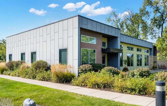 A modern building with a grey facade and greenery surrounding it.