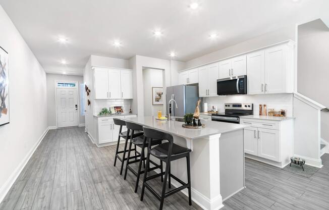 Open-concept kitchens feature expansive quartz islands with seating, white shaker-style cabinetry, stainless steel appliances, and generous prep space designed for everyday living and entertaining.