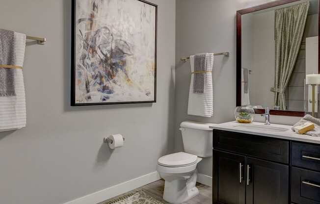 A bathroom with a toilet, sink, and a painting on the wall.