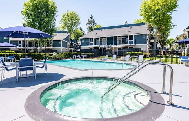 A hot tub sits in the middle of a pool surrounded by chairs and umbrellas.