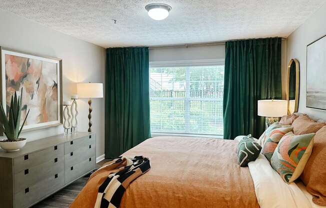 A bedroom with a bed, dresser, and window with green curtains.