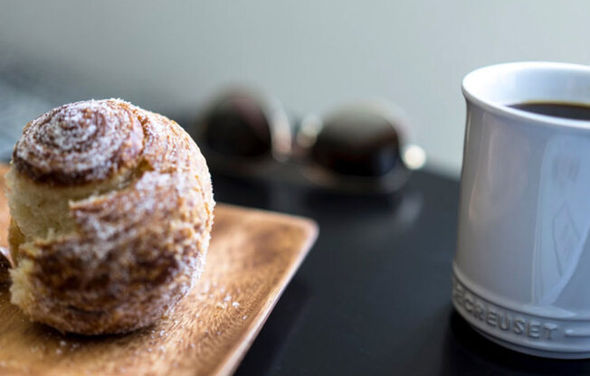 a doughnut on a cutting board next to a cup of coffee