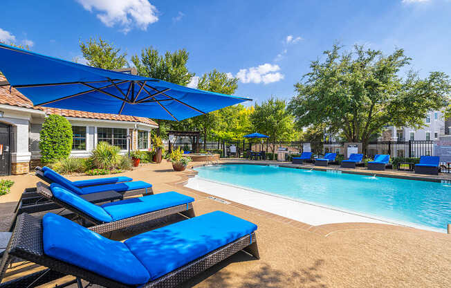 A pool area with blue lounge chairs and umbrellas.