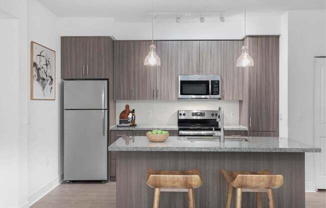 A modern kitchen with a refrigerator, microwave, oven, and a counter with two chairs.