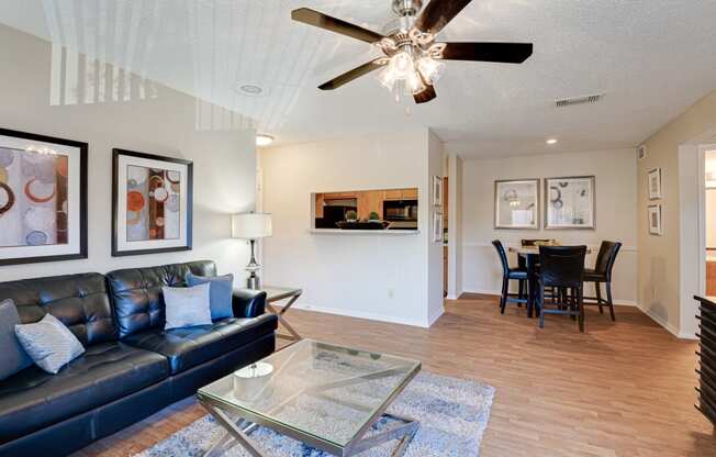 a living room with a leather couch and a glass coffee table and a dining room