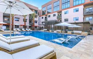 A pool with sun loungers and umbrellas in front of a building.