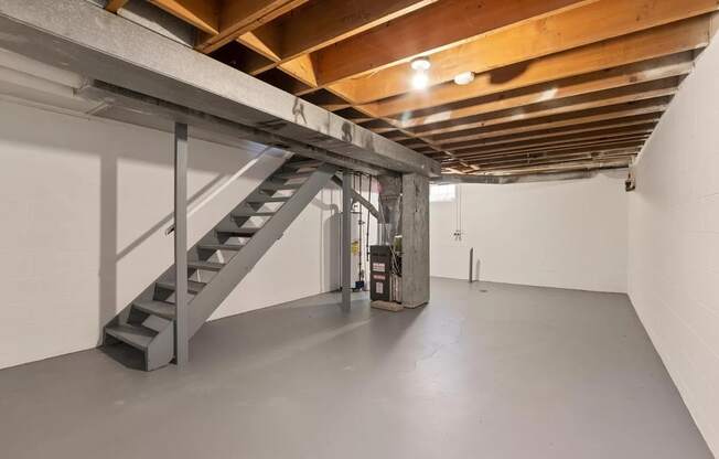 a basement with stairs and a white wall and a ceiling with wooden beams