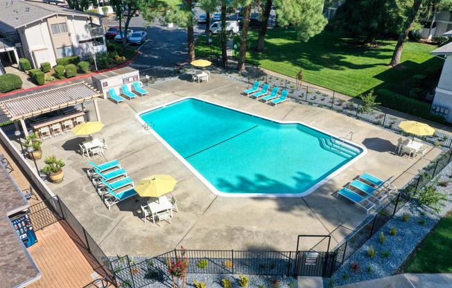 Drone photo of the community swimming pool area which is fenced and pool deck is filled with seating options. at Renaissance Park Apartments, Davis, CA, 95618