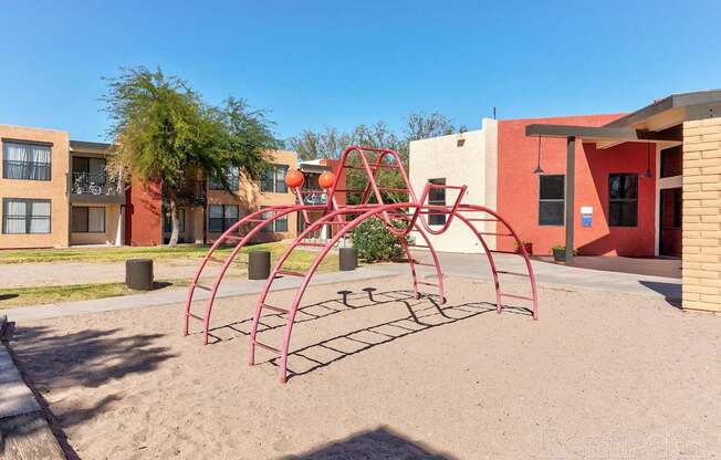 A playground with a red swing set in front of a building.