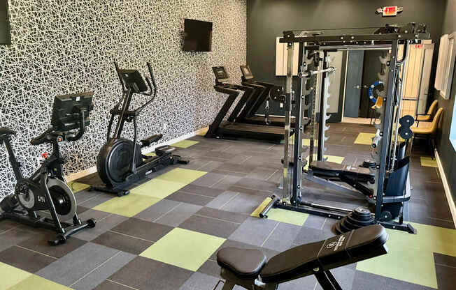 A gym with a variety of equipment including a stationary bike, a rowing machine, a bench press, and a leg press.