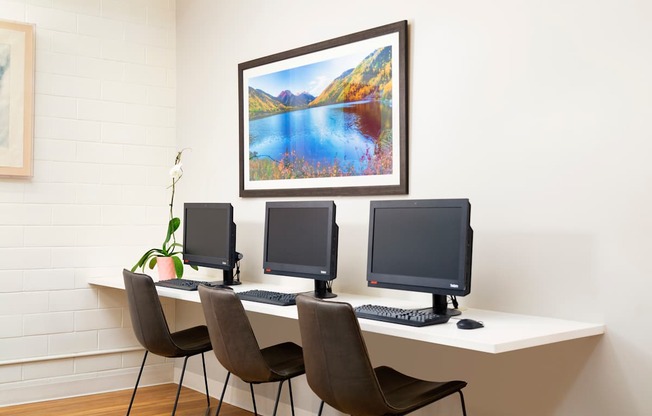 Three computer monitors are on a desk with chairs.