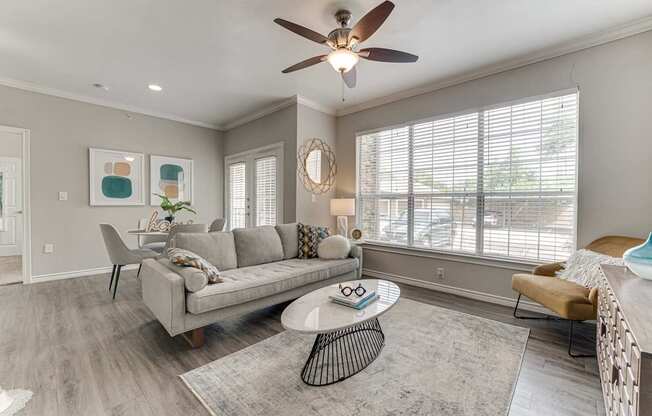 A living room with a grey couch, a round table, and a ceiling fan.