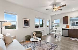 A living room with a couch, a table, a fan, and a window.