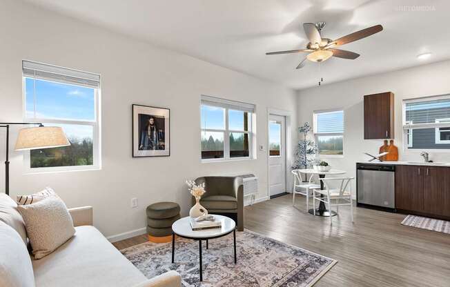 A living room with a couch, a table, a fan, and a window.