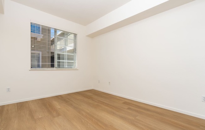 a bedroom with white walls and wood flooring and a window