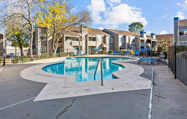 our apartments have a swimming pool with chairs and apartment buildings in the background