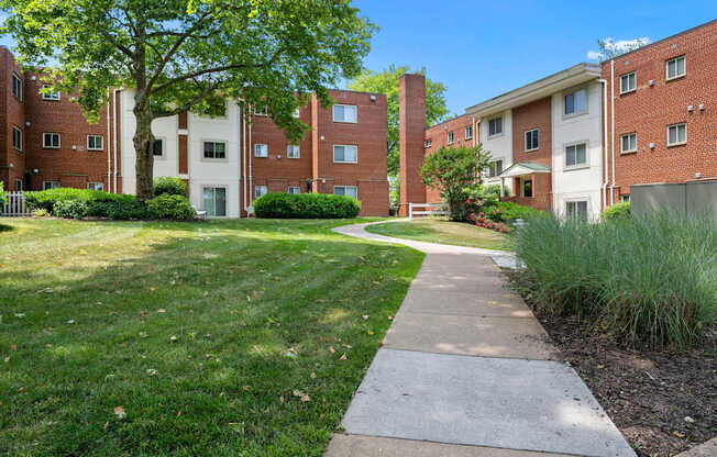 A grassy area with a concrete walkway separates two buildings.