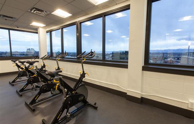a row of exercise bikes in a gym with a view of the city