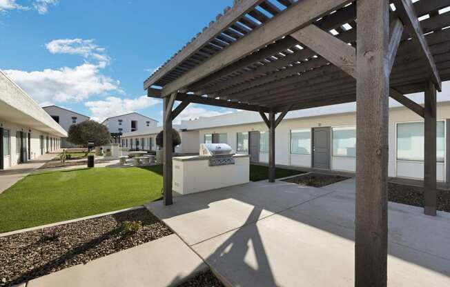 a covered patio with a grill and a lawn in front of a building
