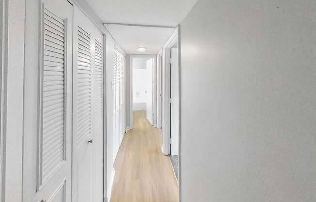 a white hallway with white shutters and a wood floor