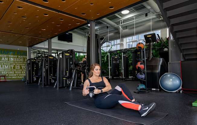 a woman sitting on a yoga mat in a gym with weights in her hands