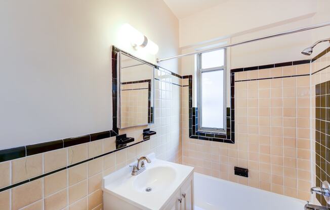 bathroom with tub, vanity, large mirror, tile details and window at baystate apartments in washington dc
