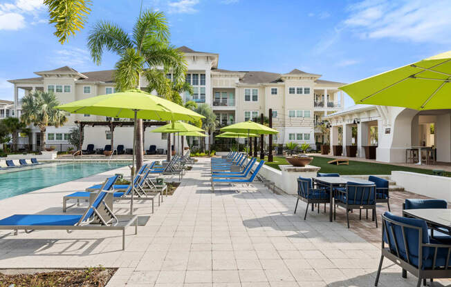 a pool with blue chairs and yellow umbrellas and buildings in the background