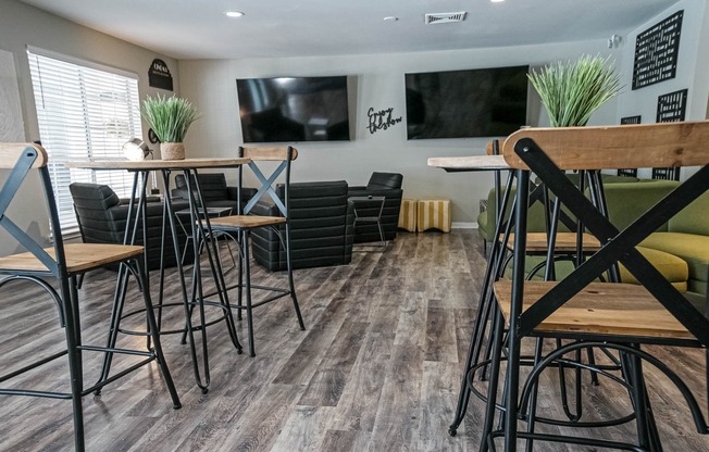 Community lounge area with sitting chairs, televisions, and hightop tables