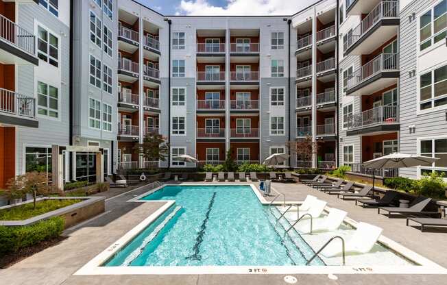 an outdoor swimming pool with lounge chairs and umbrellas in front of an apartment building  at Abberly Noda Vista Apartment Homes, North Carolina