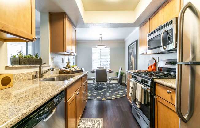 Walnut Creek, CA Apartments for Rent - Park Lake at Walnut Creek - Kitchen with Granite Countertops, Wood-Style Cabinets, Stainless Steel Appliances, Windows, a Dining Area, and Distinctive Wood-Style Flooring