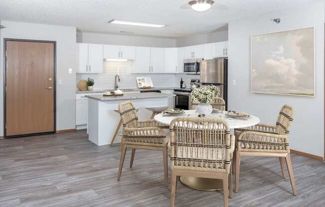 a dining area with a table and chairs and a kitchen in the background