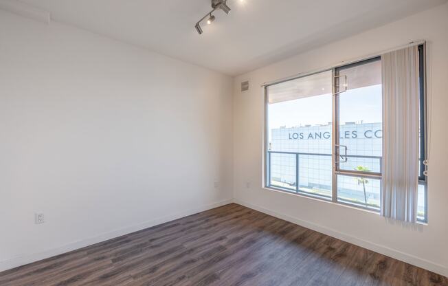 an empty living room with a large window and wood flooring