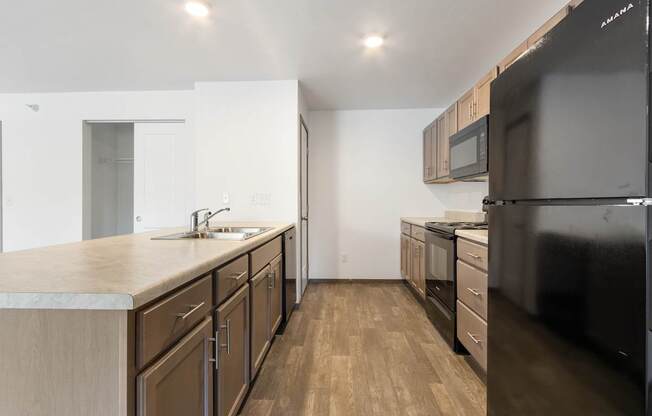 A kitchen with wooden floors and a black refrigerator.