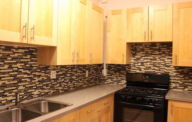 Kitchen in one bedroom brookmore apartment in Pasadena. Modern wood cabinets with silver pulls, multicolored tile backsplash, and black gas stove