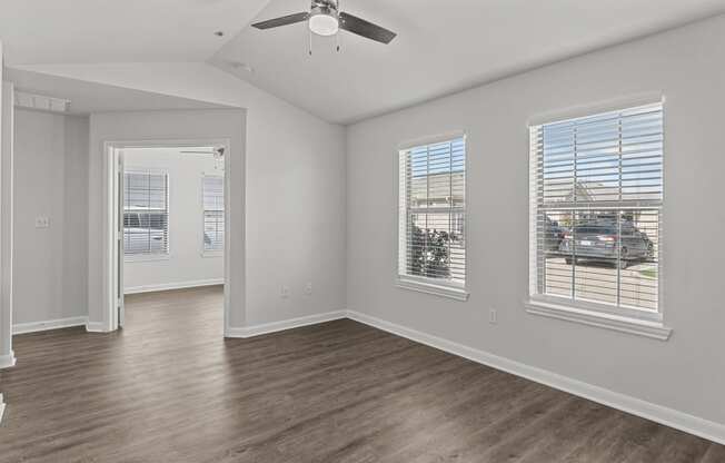 an empty living room with a ceiling fan and three windows