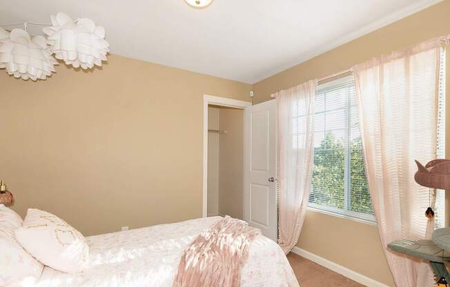 A bedroom with a bed, a window with curtains, and a chandelier at The Landing Apartments and Townhomes, Oregon, 97045