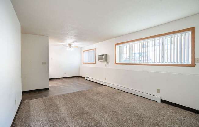 A room with a carpeted floor and a window with blinds. Fargo, ND Islander Apartments