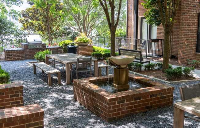 a seating area with a fountain and benches in front of a brick building