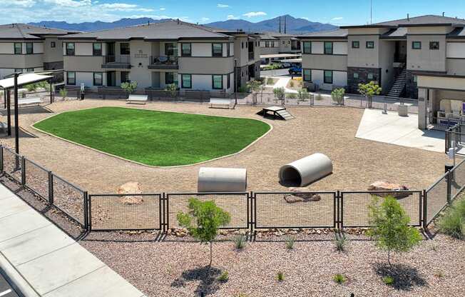 A large grassy area surrounded by a fence in front of apartment buildings.