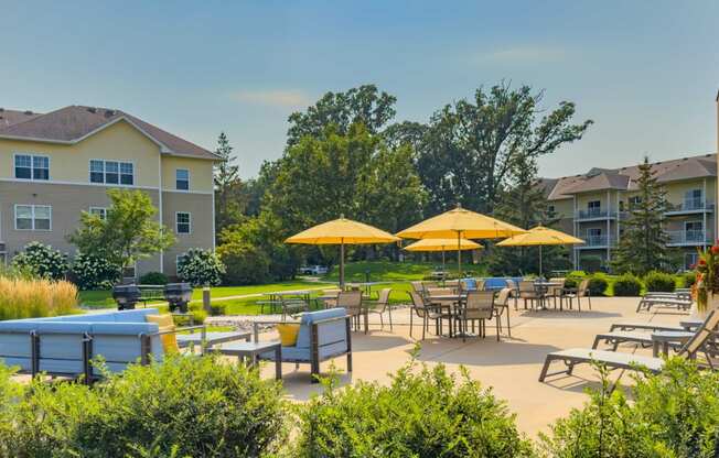 an outdoor patio with tables and umbrellas at chaska place apartments